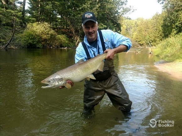 a salmon angler in waders holding a nice chinook salmon on the Manistee River