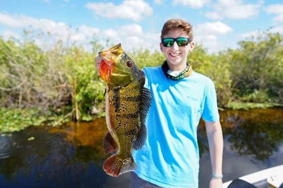a young angler on a boat holding a 5-pound peacock bass