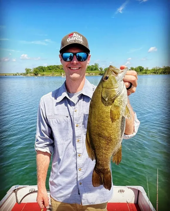 a happy fisher holding a big smallmouth bass that he has caught on a spinnerbait