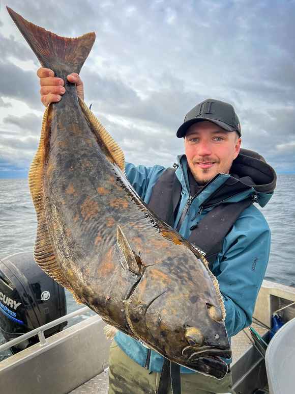a fisher on a boat holding a big halibut caught on a herring