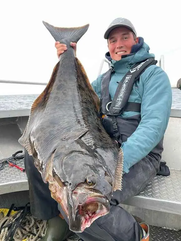 a saltwater angler holding a huge halibut off the coast of Norway