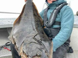 a saltwater angler holding a huge halibut off the coast of Norway