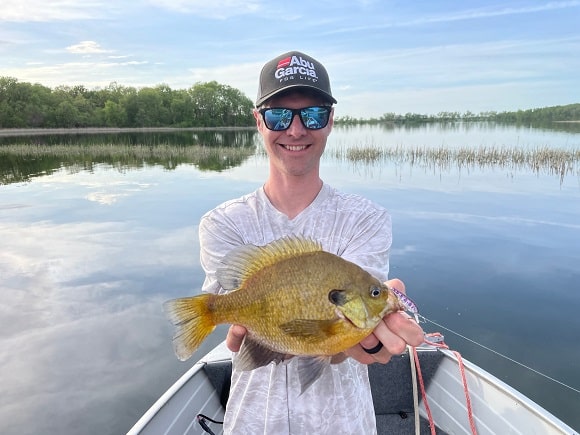 a happy angler on his boat holding a very big pre-spawn bluegill