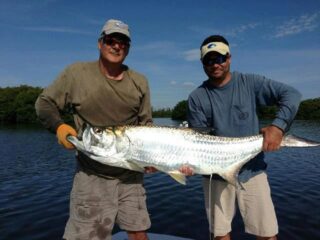 two happy anglers on a boat holding a gigantic tarpon