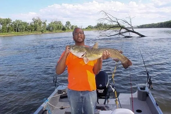 a happy angler on his boat holding a big flathead catfish
