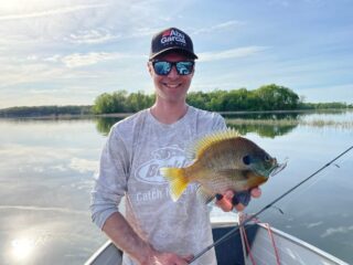a happy panfish angler on his boat holding a big clear water bluegill