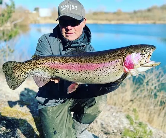 a happy trout angler holding a very big and long post-spawn rainbow trout