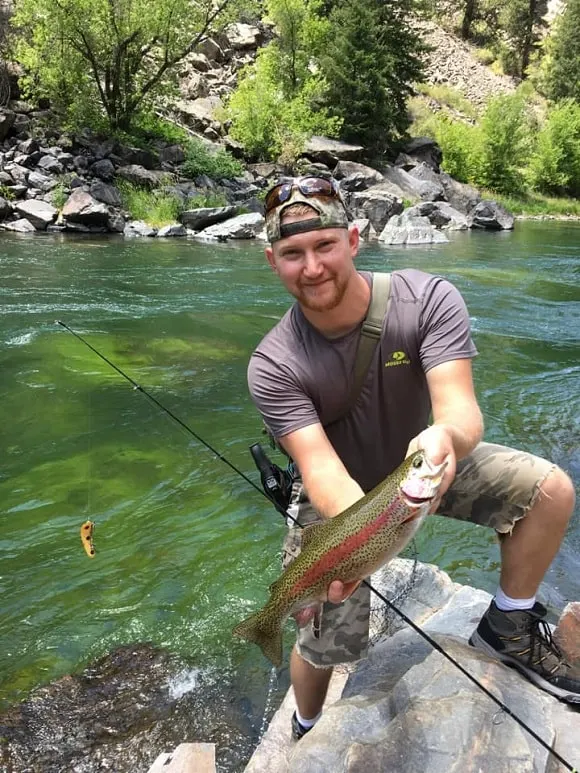 a happy angler on a fast flowing river holding a nice rainbow trout