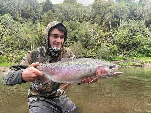 a happy fly fisherman on a river holding a giant rainbow trout