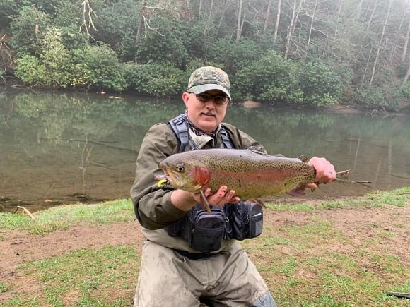 a fly fisherman with a big spring rainbow trout