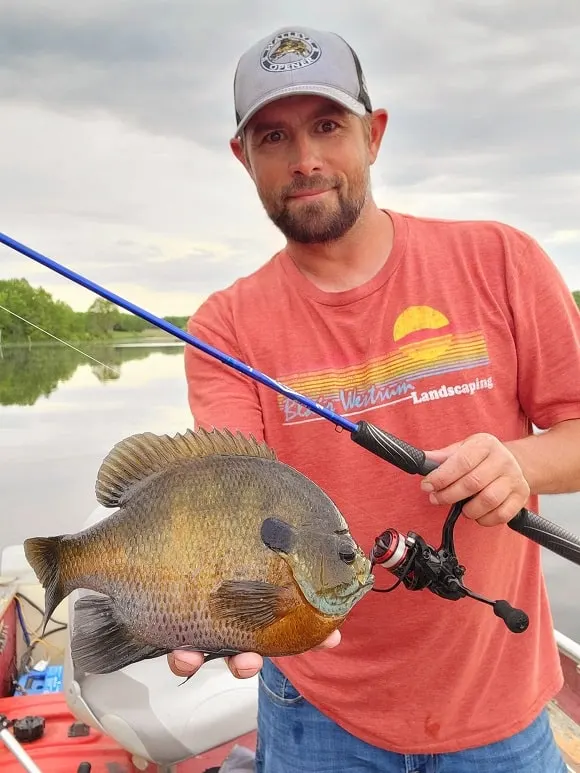 a happy angler on a lake holding a gigantic clear water bluegill