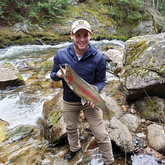 a fisher next to a creek holding a big rainbow trout caught during the spawning season