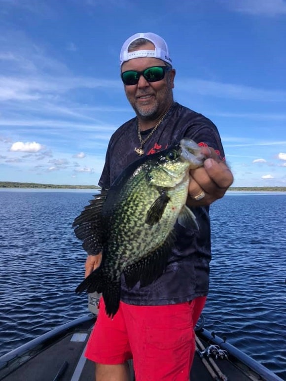a happy panfish angler on his boat holding a nice crappie that he has caught using a landing net
