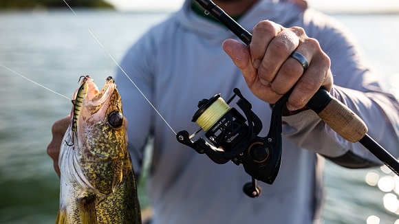 a bass angler holding a fish and a rod with a piscifun carbon x spinning reel