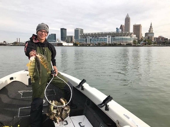 a happy angler on his boat holding a net full of yellow perch