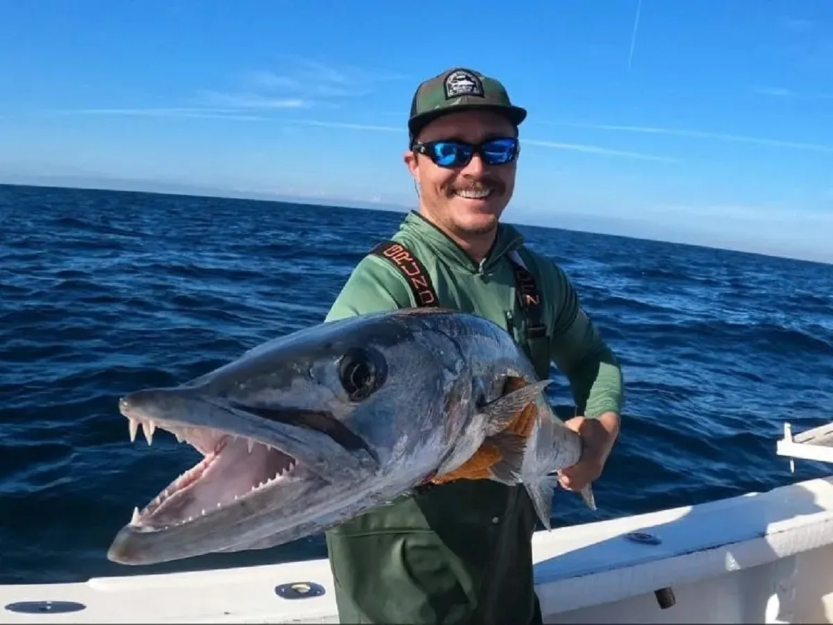 a happy saltwater angler on a boat holding a big barracuda