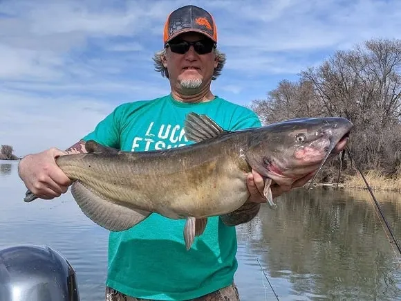 a US angler on his boat holding a big channel catfish that he has landed with a Frabill teardrop net
