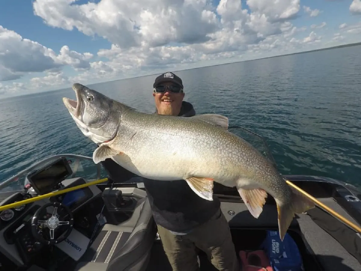 a happy angler on his boat holding a giant lake trout