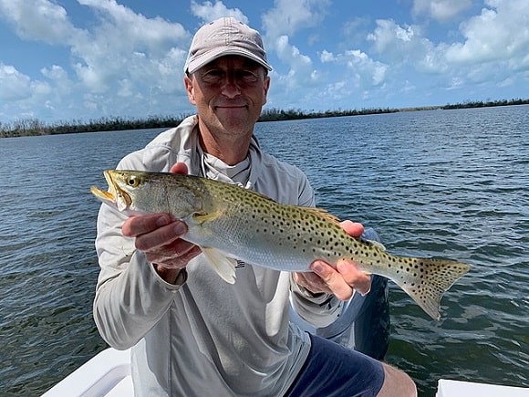 a saltwater angler on a boat holding a big speckled trout