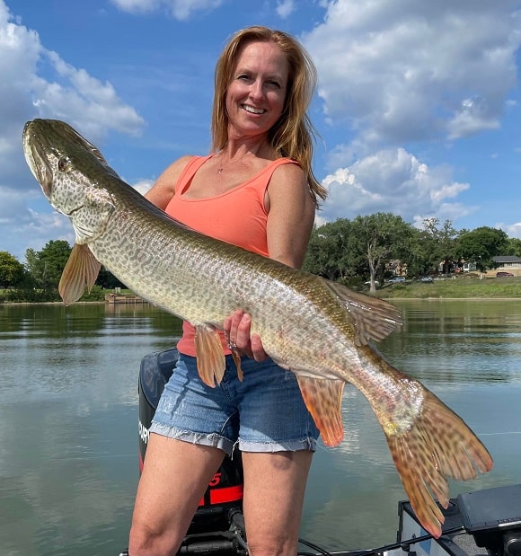 a female angler on a boat with a trophy-sized tiger musky