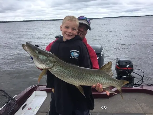 a young angler and his dad on a boat holding a nice tiger musky